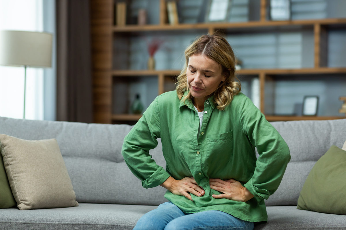  A stock image of a woman is sitting on the sofa at home, holding her stomach with her hands. 
