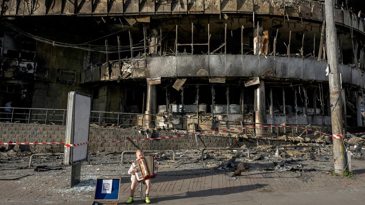 A boy plays the accordion in front of a shopping center damaged by Russian strikes in Kyiv, Ukraine, on Monday. Moscow is ramping up ballistic missile attacks on Ukraine to try to regain the strategic initiative by overwhelming air defenses and demoralizing its population.
