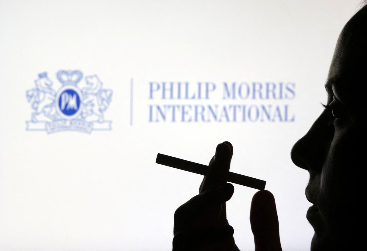 A woman poses with a cigarette in front of Philip Morris International logo in this illustration taken July 26, 2022. REUTERS/Dado Ruvic/Illustration