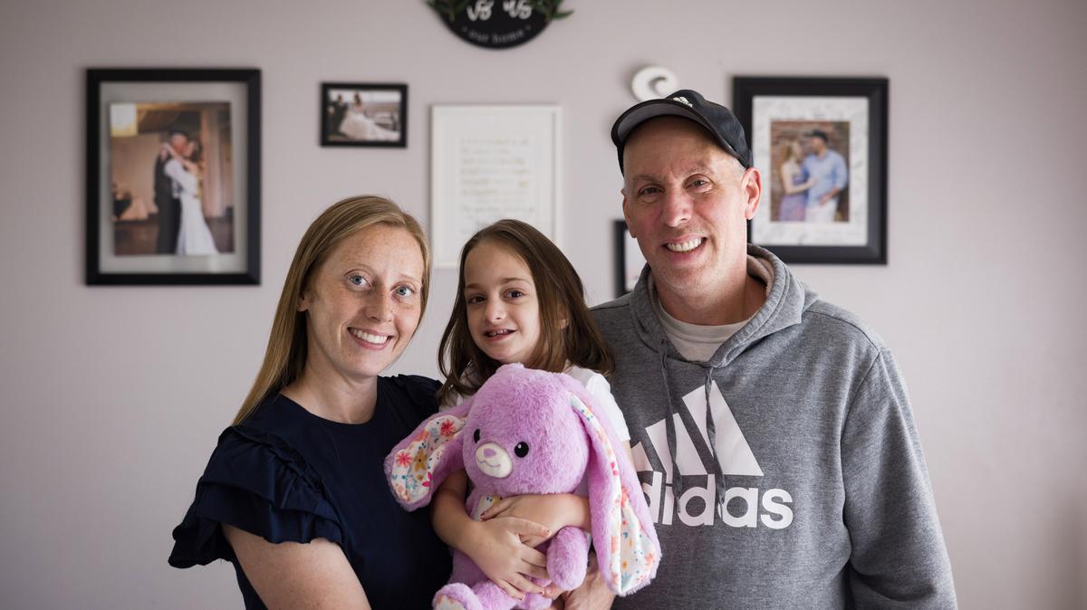 Ollie Super, 8, poses for a portrait with her adoptive parents, Britany and Jason, on Wednesday, Mar. 25, 2026, at their home in Eden, North Carolina. Ollie has moved in and out of cancer treatment since she was diagnosed with neuroblastoma as a toddler in foster care. (Allison Lee Isley for KFF Health News/TNS)