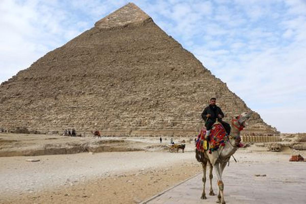 FILE PHOTO: A man waits for tourists to rent his camel in front of the Pyramid of Khufu, the largest of the Great Pyramids of Giza, on the outskirts of Cairo, Egypt January 18, 2020. REUTERS/Marius Bosch/File Photo
