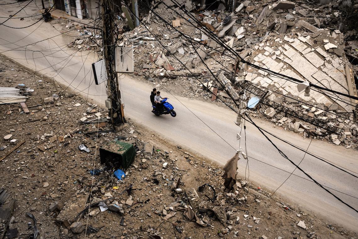 Riding on the back wheel of their motorbike, two Lebanese men pass through the ruins of the town of Chehabiyeh, Lebanon as people return to the town after the calling of a ten-day ceasefire, April 18, 2026. (David Guttenfelder/The New York Times)