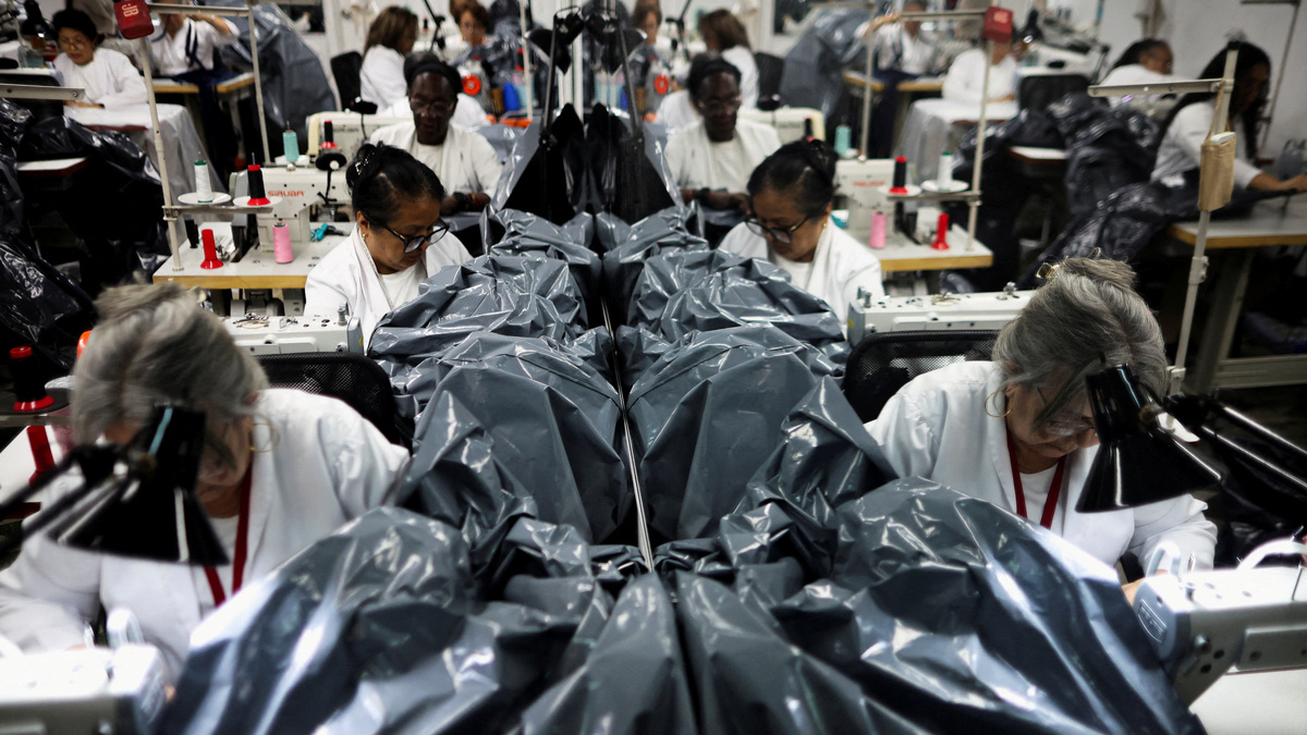 Workers make body bags, as they are reflected in a mirror, at a workshop where they are made for donation to rescue teams assisting in the recovery of victims following the June 24 earthquakes, in Maracay, Venezuela, July 7, 2026. REUTERS/Adriano Machado
