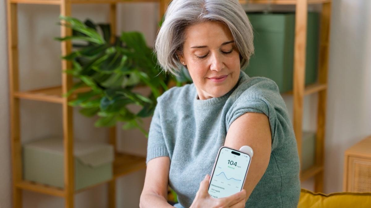 Mature adult woman reading blood sugar data from a CGM application on her mobile phone
