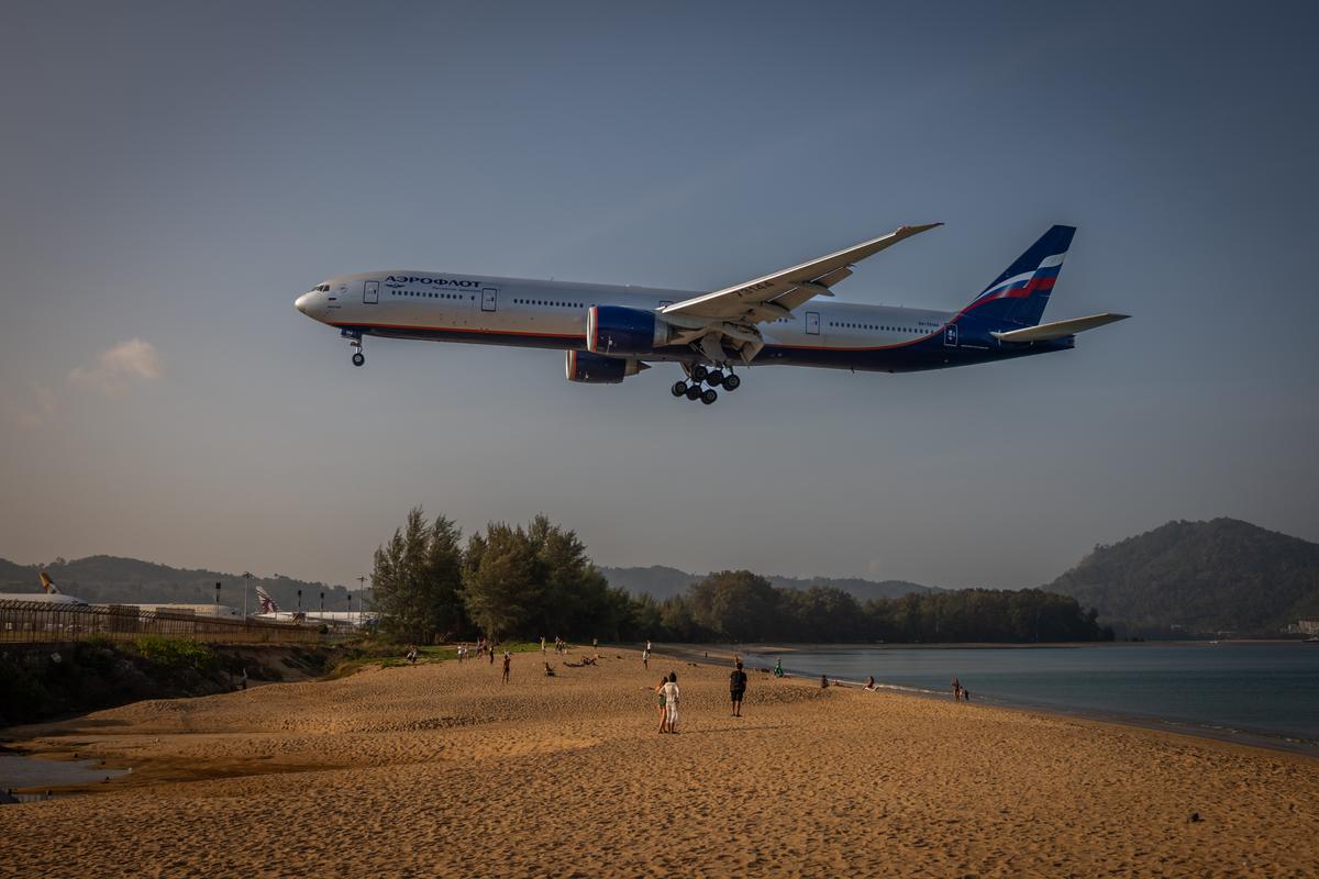 An Aeroflot plane from Moscow flies low over the beach to land in Phuket, Thailand on March 8, 2026. Thousands who fled Russia after the invasion of Ukraine have built an enclave in Phuket, where an air of impermanence hangs over their community. (Lauren DeCicca/The New York Times)..