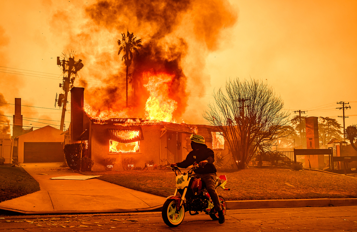 TOPSHOT - A motorcyclist stops to look at a burning home during the Eaton fire in the Altadena area of Los Angeles county, California on January 8, 2025. At least five people are now known to have died in wildfires raging around Los Angeles, with more deaths feared, law enforcement said January 8, as terrifying blazes leveled whole streets, torching cars and houses in minutes. More than 1,000 buildings have burned in multiple wildfires that have erupted around America’s second biggest city, forcing tens of thousands of people from their homes. (Photo by JOSH EDELSON / AFP) (Photo by JOSH EDELSON/AFP via Getty Images)