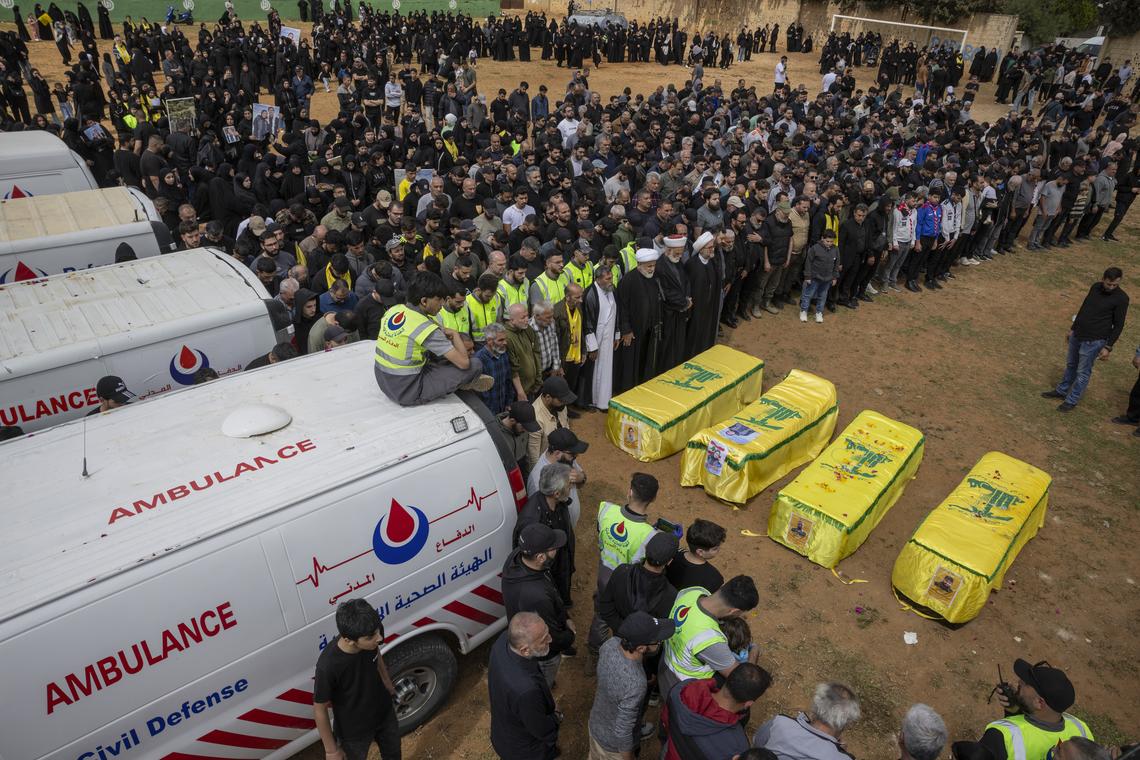 Mourners gather by coffins draped in the Hezbollah flag as a convoy of ambulances arrive in the southern Lebanese village of Bazourieh for a mass funeral, on Monday, April 20, 2026. Families gathered for the funeral of nine people -- both Hezbollah fighters and civilians -- who were killed in recent weeks (David Guttenfelder/The New York Times)