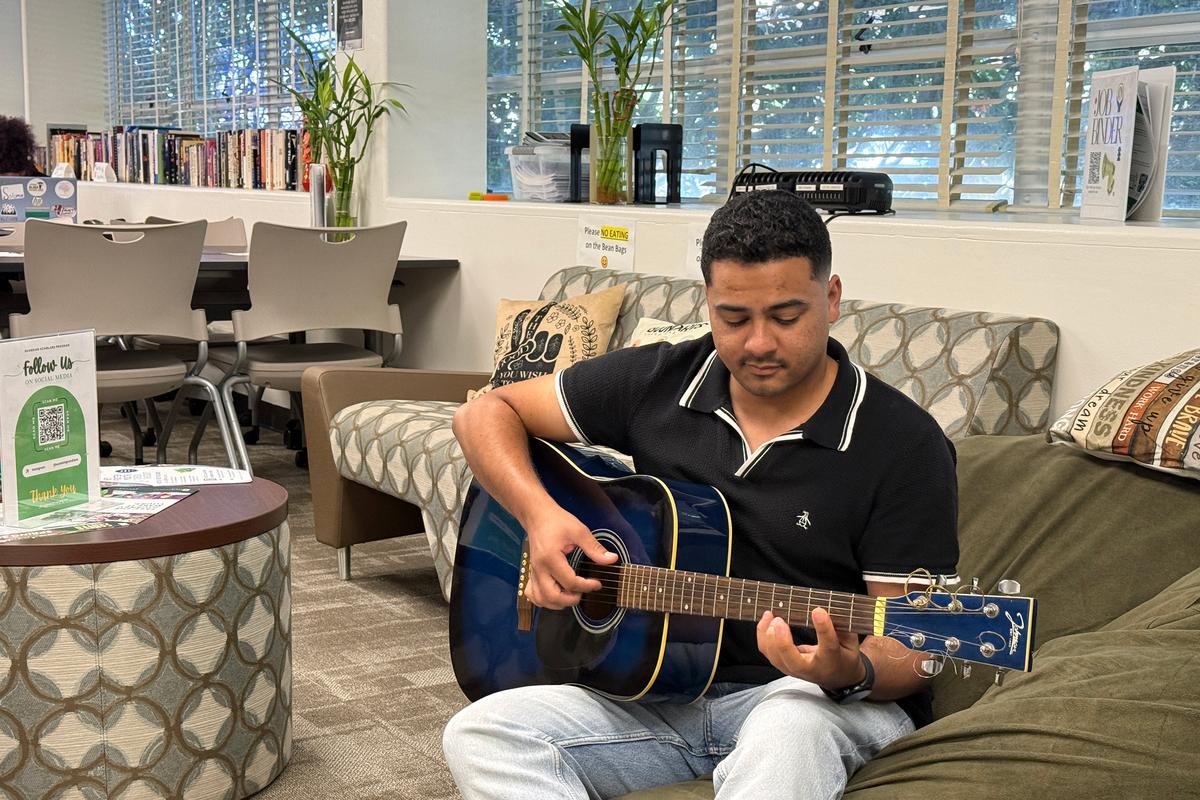  Jarred Holloway, a 26-year-old business major who is a former foster youth, strums a guitar in the Guardian Scholars Program office at California State University, Sacramento. Credit: Olivia Sanchez/The Hechinger Report