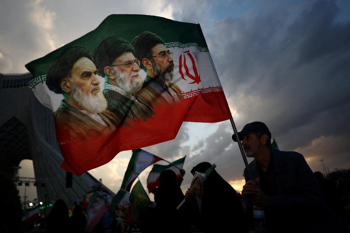 A man holds a flag with a picture of late leader of the Islamic Revolution Ayatollah Ruhollah Khomeini, late Supreme Leader of Iran Ayatollah Ali Khamenei and Iran's new Supreme Leader Mojtaba Khamenei, during a rally in Tehran, Iran, April 29, 2026. Majid Asgaripour/WANA (West Asia News Agency) via REUTERS