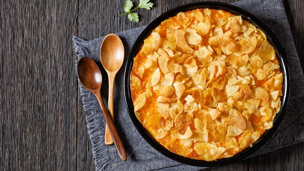 creamy cheesy chicken almond casserole topped with potato chips in baking dish on dark wooden table, american recipe, horizontal view from above, flat lay, free space