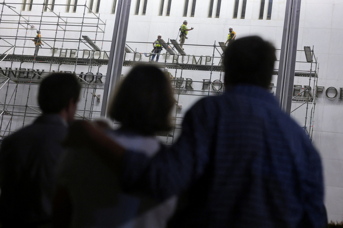 People look at workers on scaffolding preparing ahead of removing lettering from the facade of the John F. Kennedy Memorial Center for the Performing Arts, following a federal judge’s order to remove U.S. President Donald Trump's name from the institution, in Washington, D.C., U.S., June 13, 2026. REUTERS/Jonathan Ernst