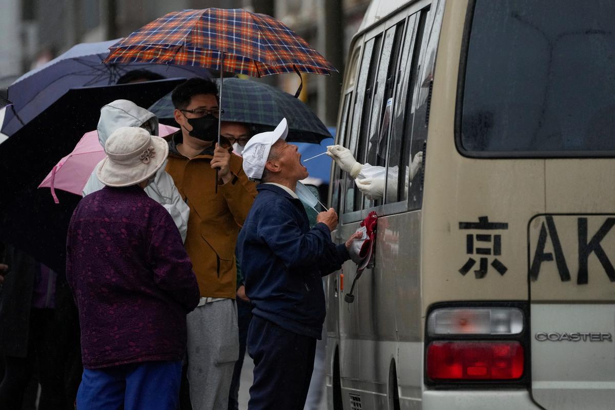 Residentes hacen fila bajo la lluvia para obtener una muestra de hisopado de garganta en un vehículo convertido en un sitio de prueba de coronavirus instalado frente a un complejo residencial, el miércoles 27 de abril de 2022 en Beijing. Los trabajadores colocaron vallas y la policía restringió quién podía salir de un área cerrada en Beijing el martes, mientras las autoridades de la capital china intensificaban los esfuerzos para prevenir un brote importante de COVID-19 como el que casi ha cerrado la ciudad de Shanghái. (Foto AP/Andy Wong)
