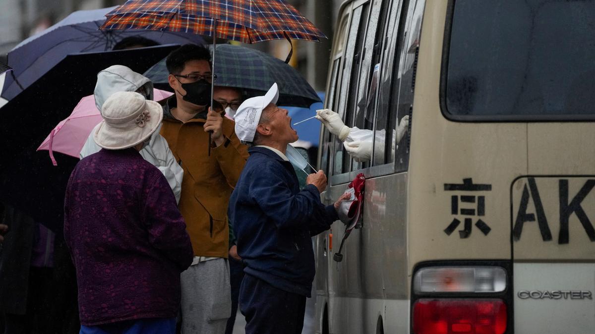 Residentes hacen fila bajo la lluvia para obtener una muestra de hisopado de garganta en un vehículo convertido en un sitio de prueba de coronavirus instalado frente a un complejo residencial, el miércoles 27 de abril de 2022 en Beijing. Los trabajadores colocaron vallas y la policía restringió quién podía salir de un área cerrada en Beijing el martes, mientras las autoridades de la capital china intensificaban los esfuerzos para prevenir un brote importante de COVID-19 como el que casi ha cerrado la ciudad de Shanghái. (Foto AP/Andy Wong)