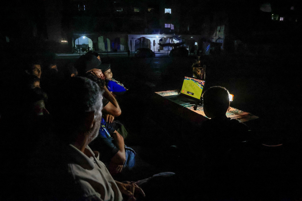Former Palestinian soccer player Fadi Al-Arawi watches a 2026 World Cup match streamed on a laptop alongside others in Khan Younis, in the southern Gaza Strip, June 13, 2026. REUTERS/Haseeb Alwazeer