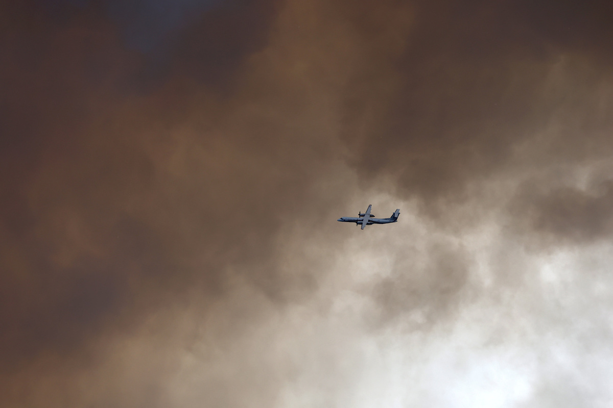 A Dash firefighting aircraft flies through plumes of smoke above the Fontainebleau forest as a wildfire burns near Paris during a heatwave affecting large parts of France, July 13, 2026. REUTERS/Stephane Mahe