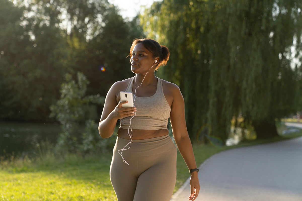  A woman uses her mobile phone and earphones while walking in the park on a summer day. 
