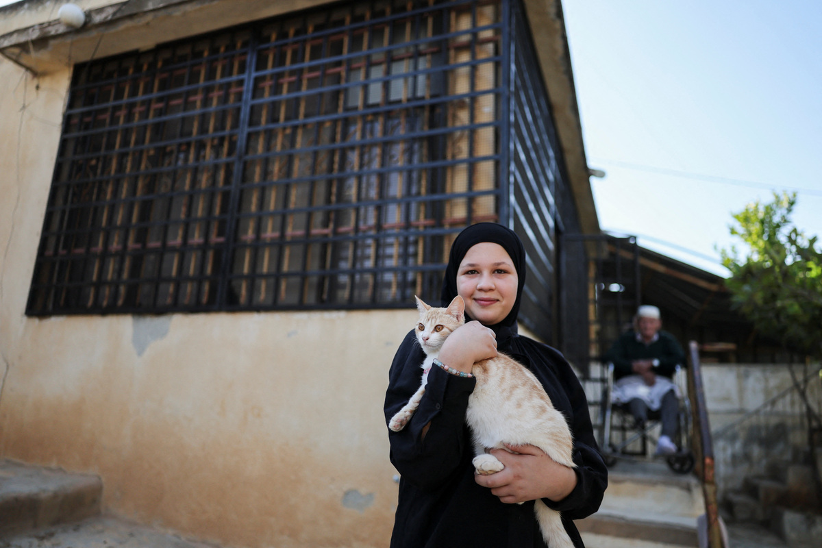 Amal Foqahaa, 13, holds a cat outside her family home, whose windows they barred after Israeli settlers threw a Molotov cocktail inside two years ago while the family was home, in Sinjil, near Ramallah, in the Israeli-occupied West Bank, June 26, 2026. REUTERS/Ammar Awad