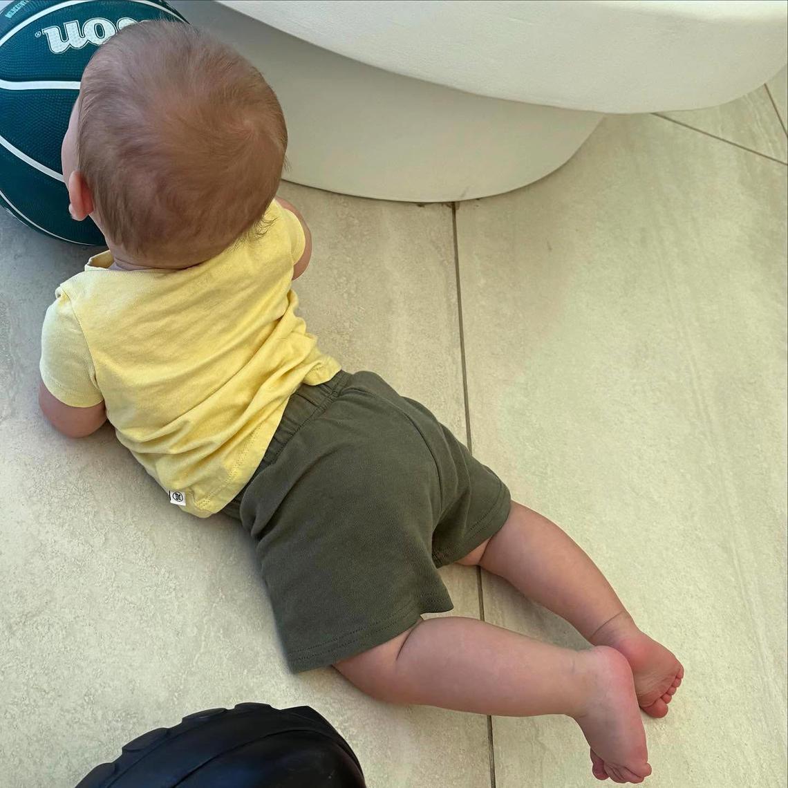 Tummy Time Baby Jack relaxed on his stomach while wearing a bright yellow shirt and a pair of green shorts. Courtesy of Justin Bieber/Instagram