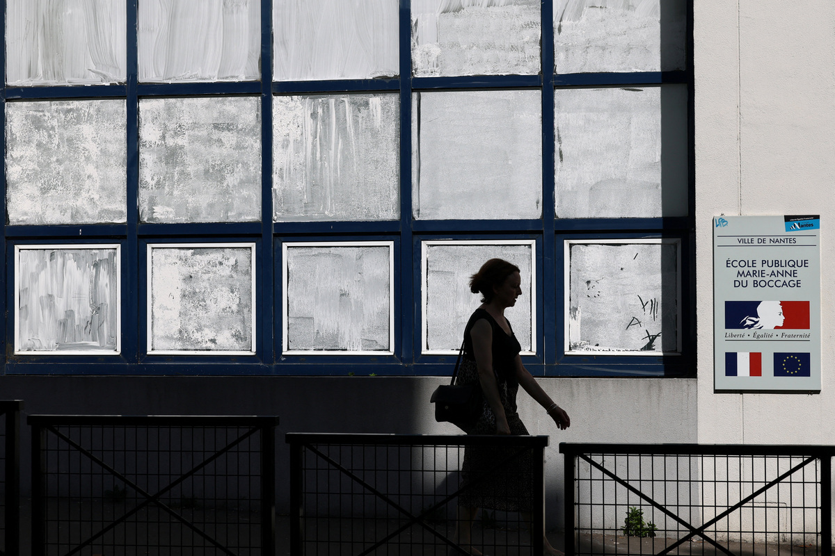 A woman walks past the public school Marie-Anne du Boccage with windows coated in Blanc de Meudon, a chalk-based powder applied by parents to protect their children from the heat in Nantes, during a heatwave affecting a majority of the country, France, June 25, 2026. REUTERS/Stephane Mahe
