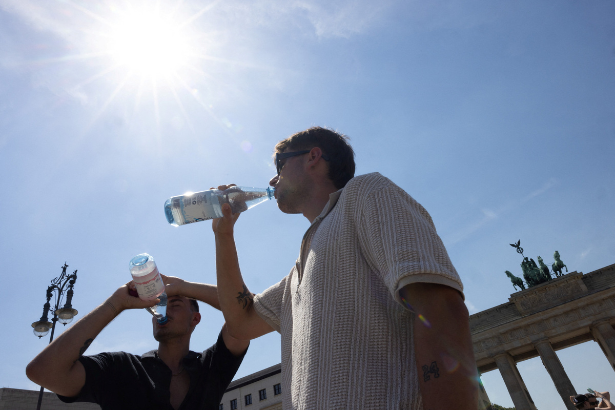 Men drink water in front of the Brandenburg Gate during the ongoing heatwave in Berlin, Germany, June 27, 2026. REUTERS/Axel Schmidt