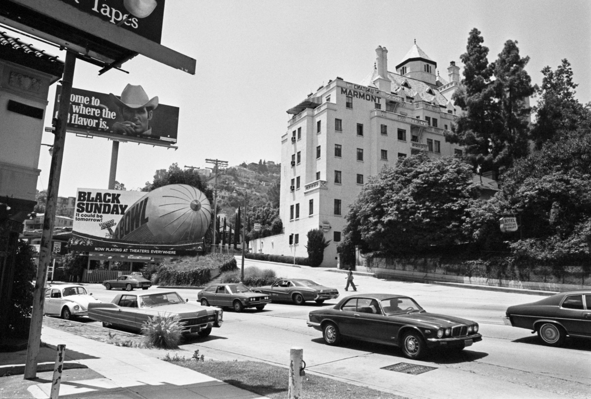  Traffic passes along Sunset Boulevard, passing beneath billboards advertising ‘Black Sunday’ and Marlboro cigarette with the Chateau Marmont hotel on the far side of the road, in Los Angeles, California, June 1977. Designed by architects Arnold A Weitzman and William Douglas Lee, the building is loosely based on the Chateau d’Amboise, a country house in the Loire Valley. 