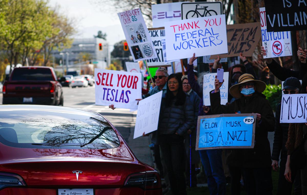 A Tesla drives by as people protest against Elon Musk on Saturday in San Jose, California.