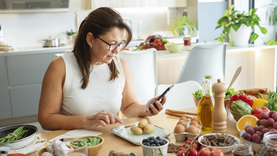 Woman in kitchen using weight scale to plan well balanced diet.