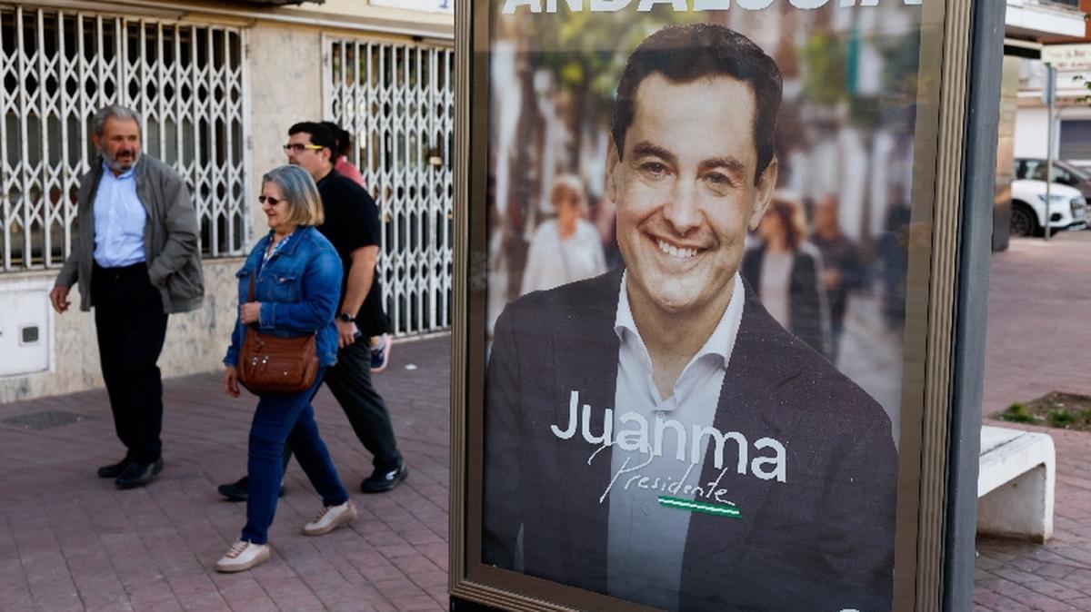 People walk past an electoral poster of Andalusian regional president and People's Party (PP) candidate, Juanma Moreno Bonilla, during the Andalusian regional elections in Ronda, Spain May 17, 2026. REUTERS/Jon Nazca