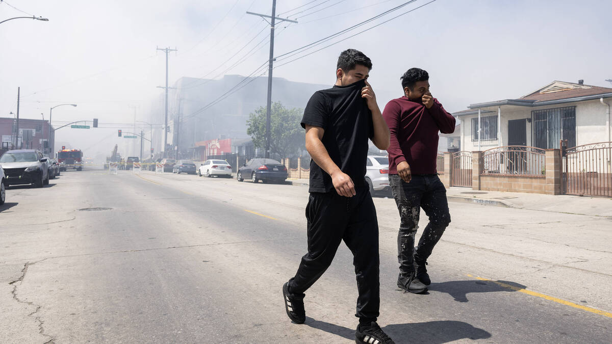 From left, Fernando Perez and Antonio Perez cover their faces as they try to avoid toxic smoke spewing from a cold storage facility in Boyle Heights on Monday, June 22, 2026. (Photo by Drew A. Kelley, Press-Telegram/SCNG)