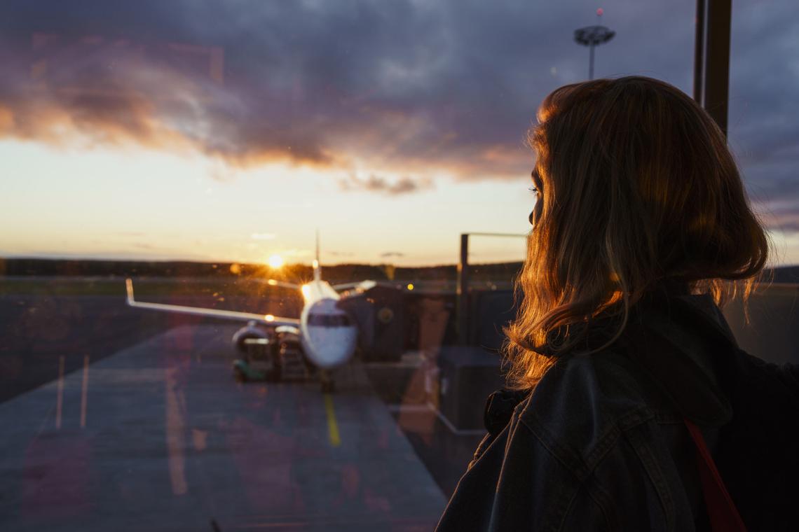  A quiet moment of a person standing at a large airport window, thoughtfully observing an aircraft outside. Stock photo via Getty Images 
