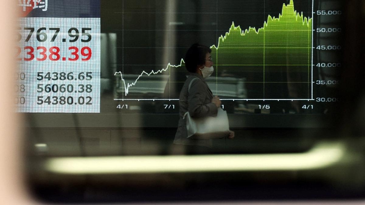 A woman walks past a screen displaying Japan's Nikkei share average and a graph showing recent movements of the average, outside a brokerage in Tokyo, Japan April 8, 2026. REUTERS/Issei Kato