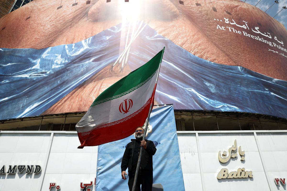 A man holds an Iranian flag near an anti-U.S. billboard depicting U.S. President Donald Trump and the Strait of Hormuz, in Tehran, Iran, May 2, 2026. Majid Asgaripour/WANA (West Asia News Agency) via REUTERS