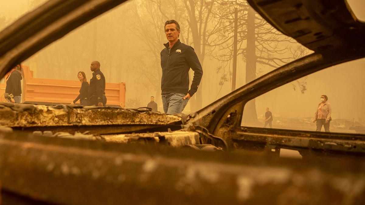California Governor Gavin Newsom (center) walks by a burned vehicle in downtown Greenville, California on Aug. 7, 2021. (Josh Edelson/AFP via Getty Images/TNS)