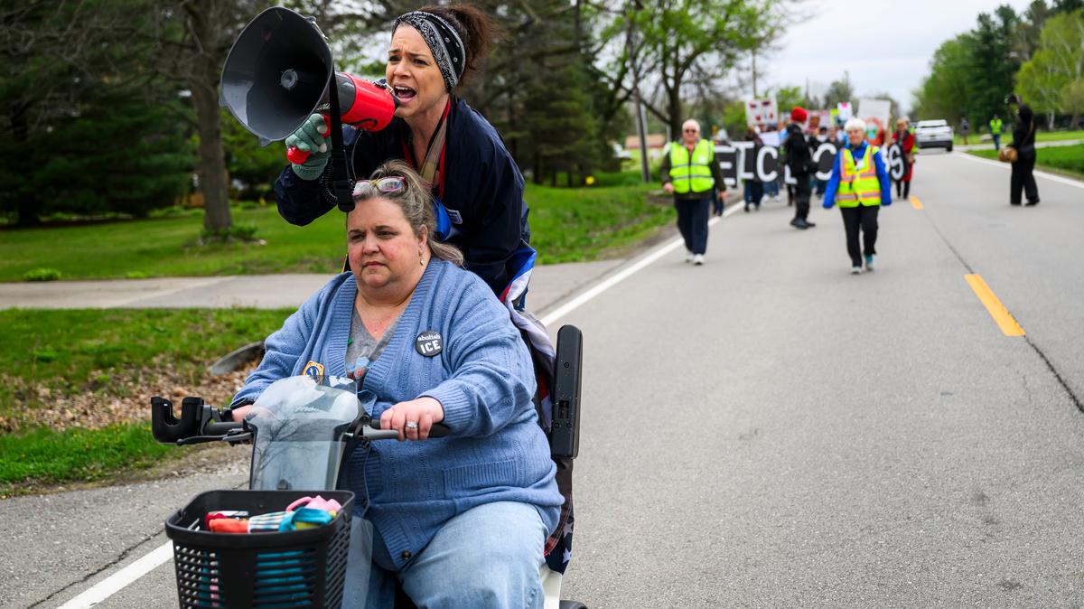 Jessica Schering of Trenton, 41, chants through a megaphone while riding on the back of a scooter driven by Ashley Perry of Riverview, 49, as they lead hundreds of people in a march in opposition to a proposed ICE facility in Romulus on Saturday, April 25, 2026, in Romulus, Michigan. (Katy Kildee/The Detroit News/TNS)