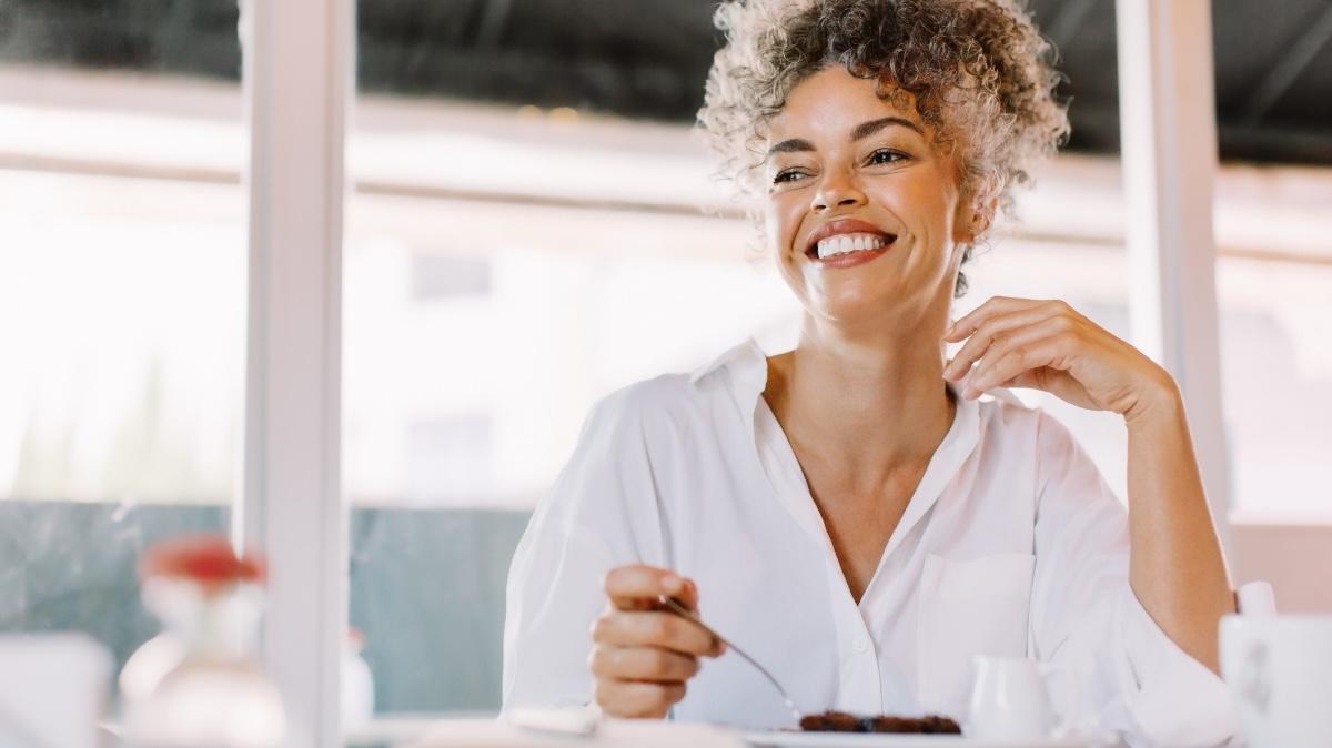 Happy mature woman looking away with a smile on her face. Mature woman having some cake while sitting at a cafe table. Cheerful woman having lunch alone in a cafe.