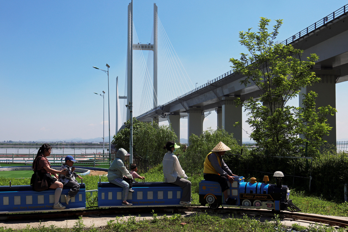 People sit on an amusement ride near the New Yalu River Bridge designed to connect China's Dandong New Zone and North Korea's Sinuiju, in Dandong, Liaoning province, China June 8, 2026. REUTERS/Maxim Shemetov