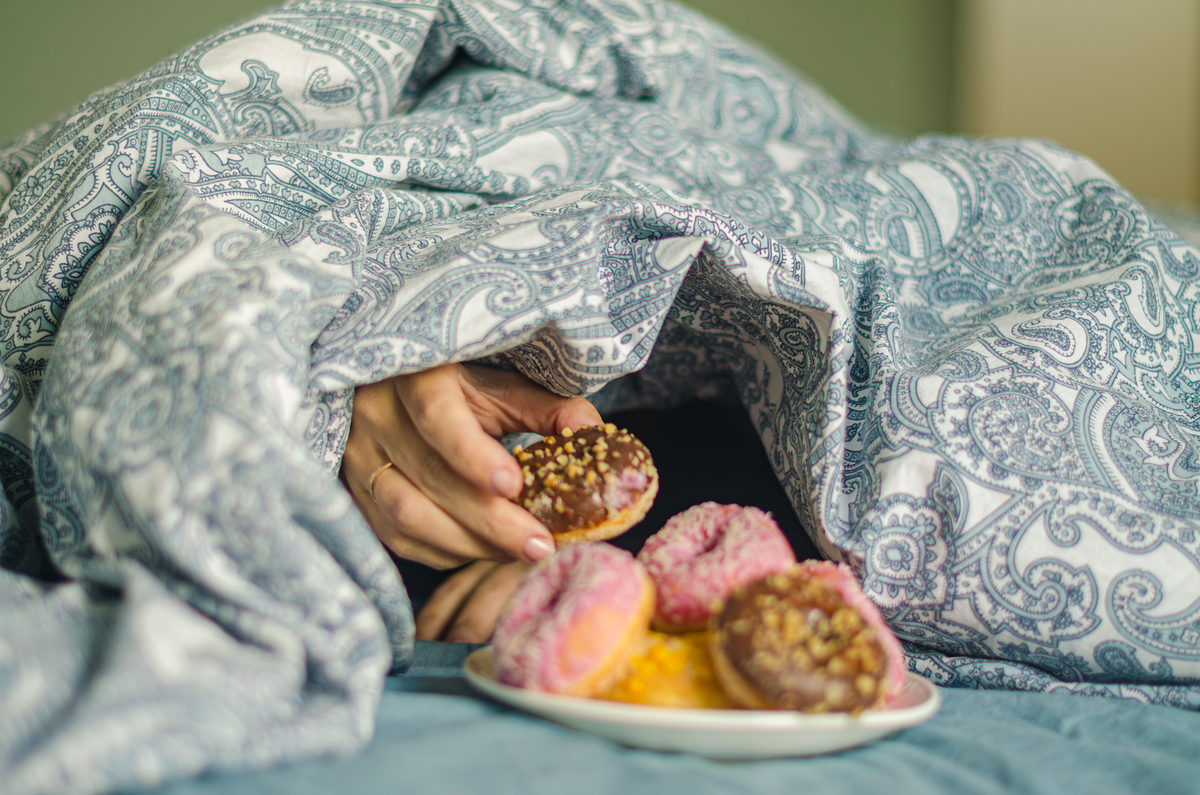  A stock image of a woman reaching hand for a doughnut while lying in bed. 