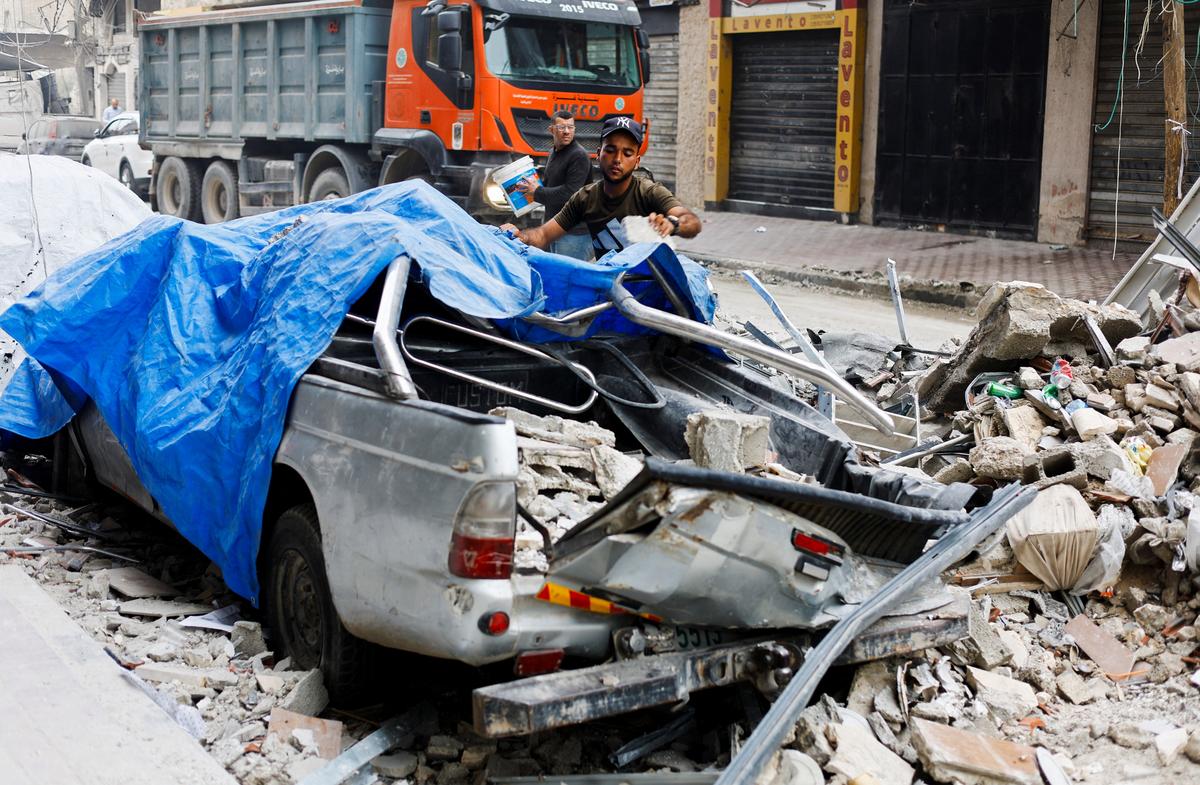 A Palestinian man moves debris next to a destroyed vehicle as he inspects the site of an Israeli airstrike on a residential building on Tuesday, in Gaza City, May 27, 2026. REUTERS/Mahmoud Isaa