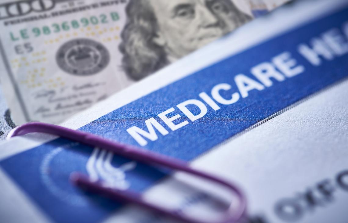  Photo illustration of a Medicare card and a $100 bill clipped to a medical report. 