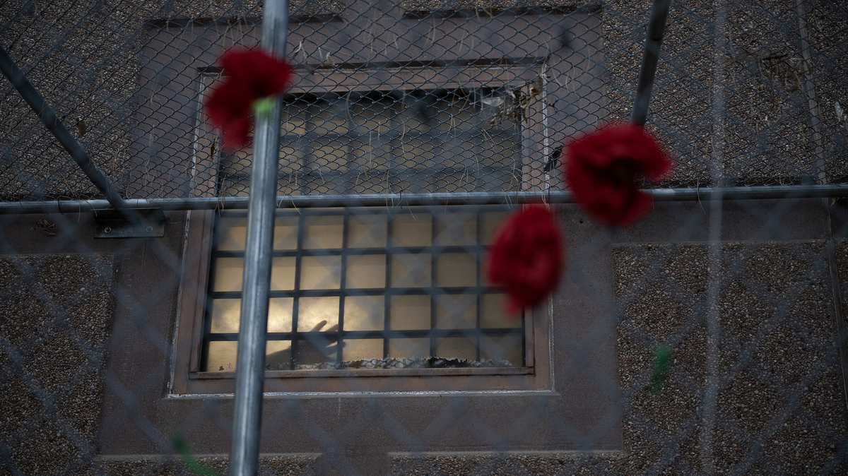 Red poppies are hung on the fence as a detainee places their hands against a window of the Aurora ICE Processing Center during a Passover Grief Vigil on April 8, 2026, in Aurora, Colorado. (Timothy Hurst/The Denver Post/TNS)