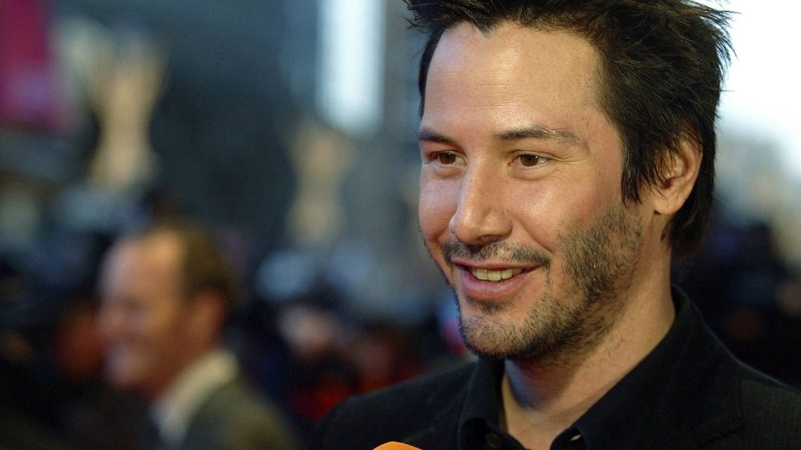 Keanu Reeves Is a Silver Fox With Shaggy Hair and a Gray Beard While Playing Chess Onstage 