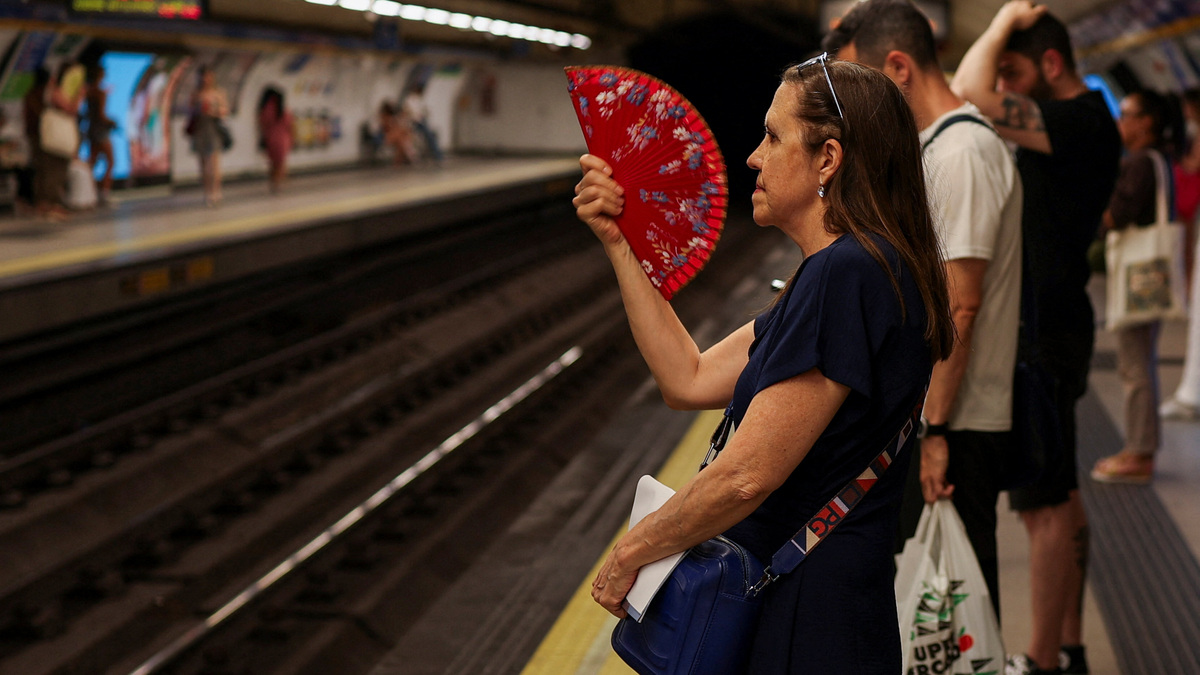 A woman uses a fan, as commuters wait to board a metro on a hot day in Madrid, Spain June 21, 2026. REUTERS/Mohammed Salem