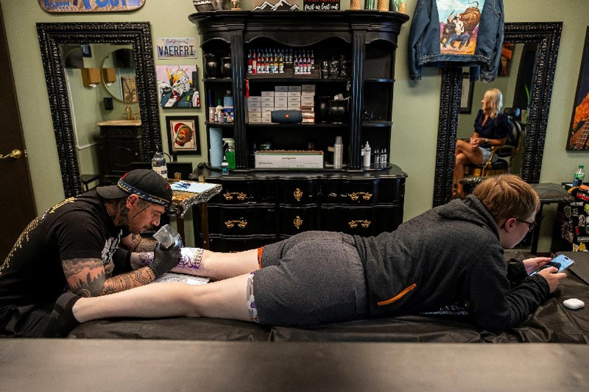 Randolph Torres tattoos the leg of Lexys Siebrands as Lexys' mother Jyl Siebrands watches in Fort Morgan, Colorado, U.S., May 11, 2026.  REUTERS/Kevin Mohatt