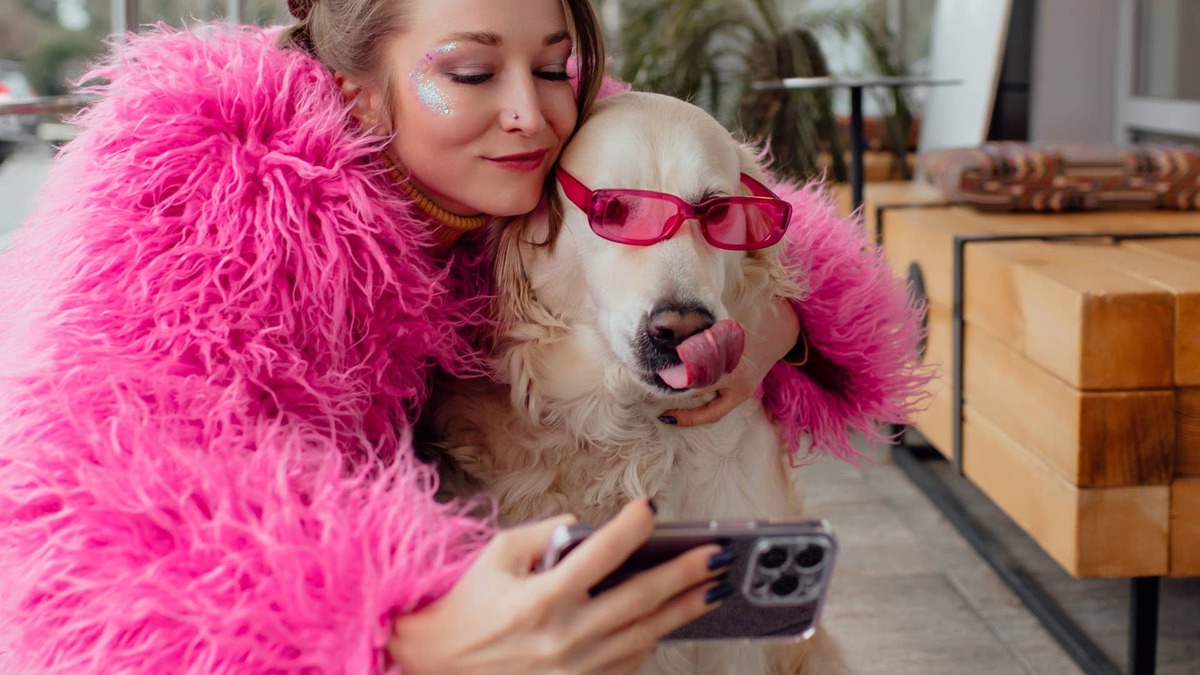 A woman takes a selfie with a Golden Retriever who's sporting sunglasses.