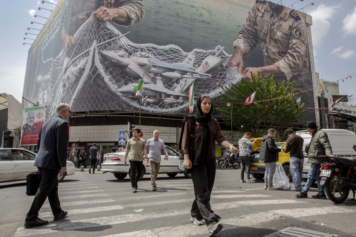 People pass near a billboard depicting American aircraft in a net in Enghelab Square in Tehran, April 20, 2026. A British-French plan to secure the Strait of Hormuz would give the continent a role. But Tehran and Washington are still calling the shots. (Arash Khamooshi/The New York Times)