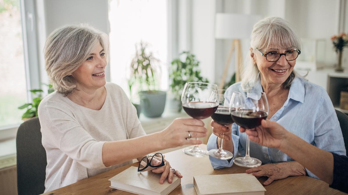Three women discussing a book and drinking red wine. Book club friends sitting at the table home.