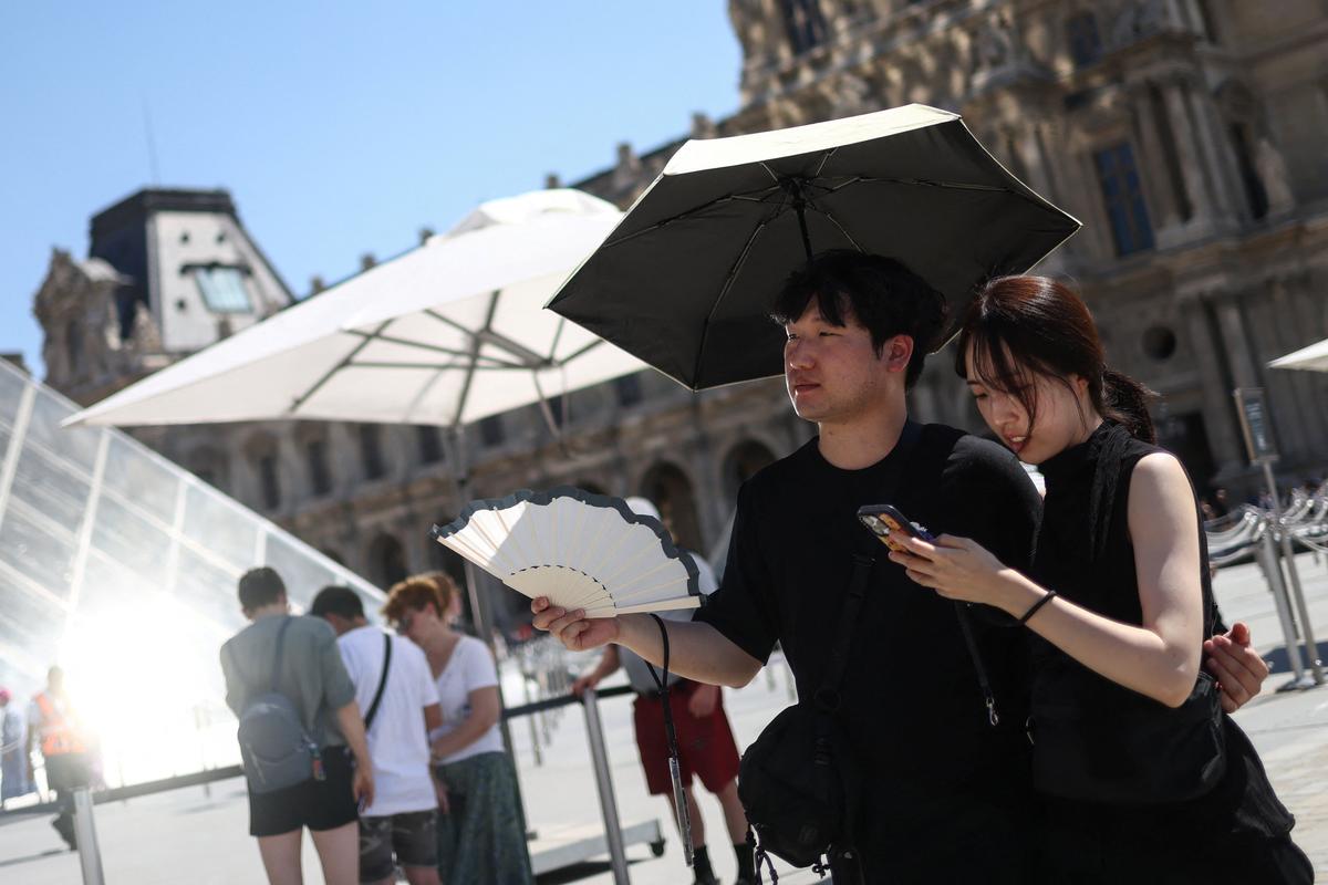 Two people shelter under an umbrella and use a fan outside the Louvre amid a severe heat wave in Paris, France, May 27, 2026. REUTERS/Tom Nicholson