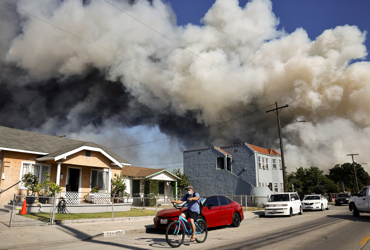  A person rides a bicycle as a massive warehouse fire at a cold storage facility continues to burn and spread smoke around the city on June 20, 2026 in Los Angeles, California. 