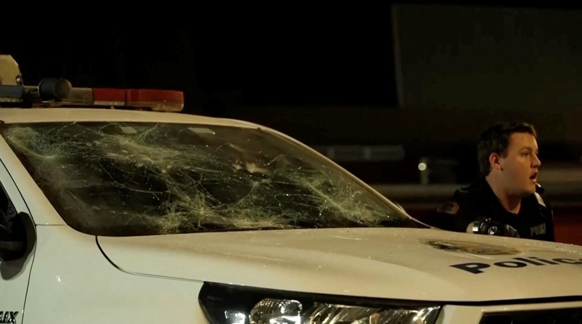 A police officer reacts next to a damaged police vehicle amidst community unrest outside Alice Springs Hospital, where a 47-year-old man arrested in connection with the alleged killing of five-year-old Kumanjayi Little Baby was taken, in Alice Springs, Australia, April 30, 2026, in this screengrab taken from a video. AUSTRALIAN BROADCASTING CORPORATION/via REUTERS