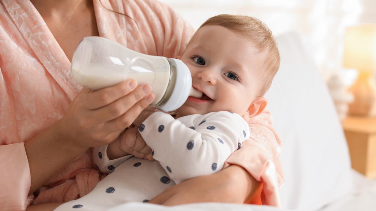 Mother feeding her little baby from bottle on bed at home, closeup. 